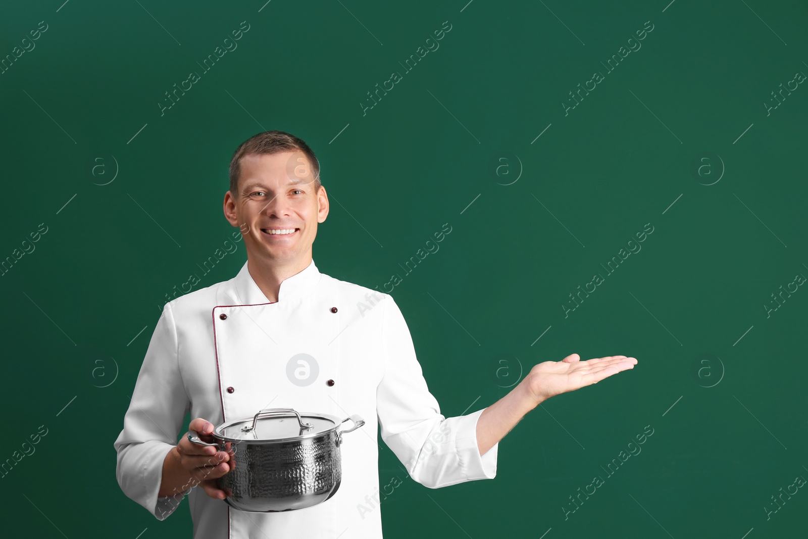 Photo of Happy male chef with cooking pot on dark green background. Space for text