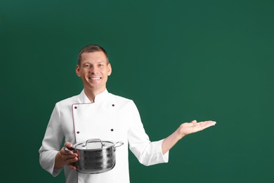 Photo of Happy male chef with cooking pot on dark green background. Space for text