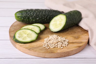 Photo of Pile of vegetable seeds and fresh cucumbers on white wooden table