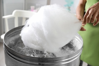 Photo of Woman making cotton candy using modern machine indoors, closeup