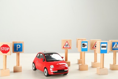 Photo of Many different miniature road signs and car on white wooden table, space for text. Driving school