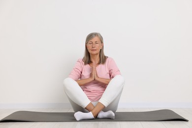 Photo of Senior woman practicing yoga on mat near white wall