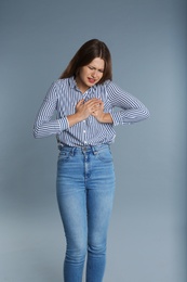 Woman suffering from chest pain on grey background