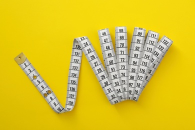 Photo of White measuring tape on yellow background, top view