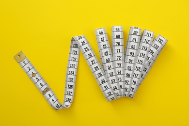 White measuring tape on yellow background, top view