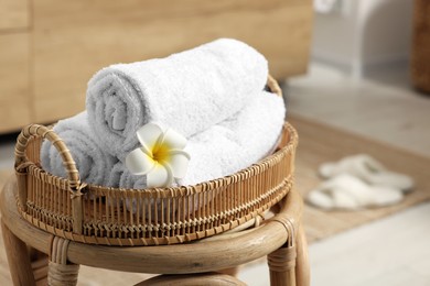 Photo of Rolled towels on wicker stool in bathroom. Space for text