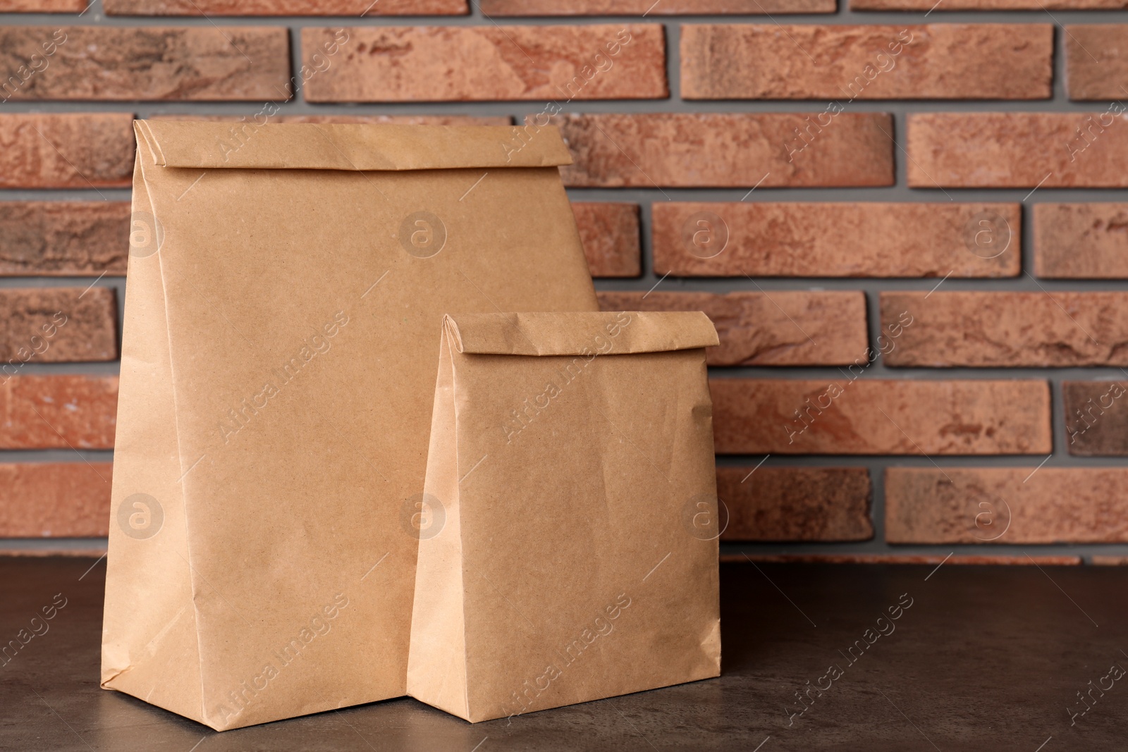 Photo of Paper bags on table against brick wall. Mockup for design