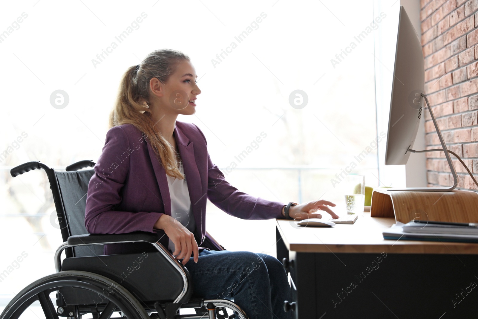 Photo of Woman in wheelchair working with computer at table indoors