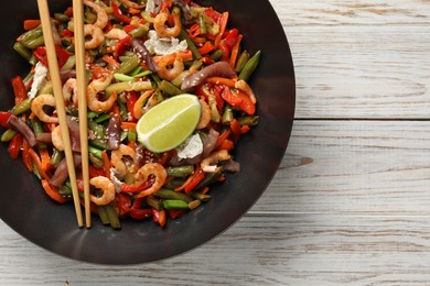 Photo of Shrimp stir fry with vegetables in wok and chopsticks on light wooden table, top view