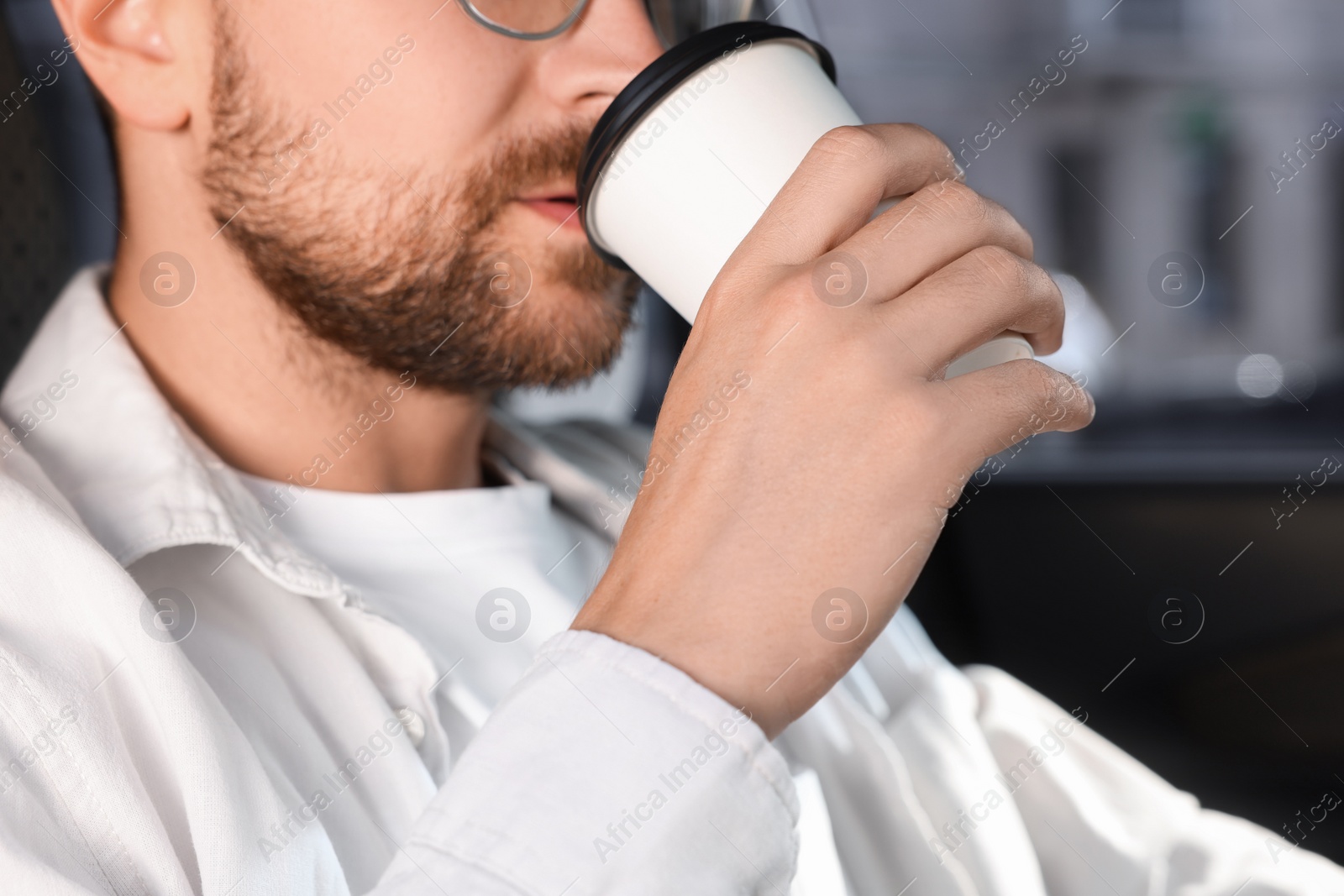 Photo of To-go drink. Man drinking coffee in car, closeup