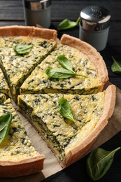 Photo of Sliced delicious homemade spinach pie on black wooden table, closeup