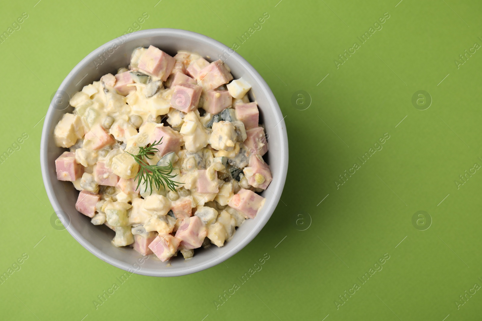 Photo of Tasty Olivier salad with boiled sausage in bowl on green table, top view. Space for text