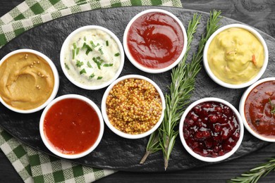 Photo of Different tasty sauces in bowls and rosemary on black wooden table, top view