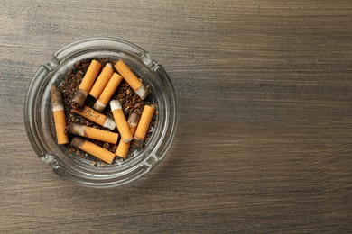 Photo of Glass ashtray with cigarette stubs on wooden table, top view. Space for text