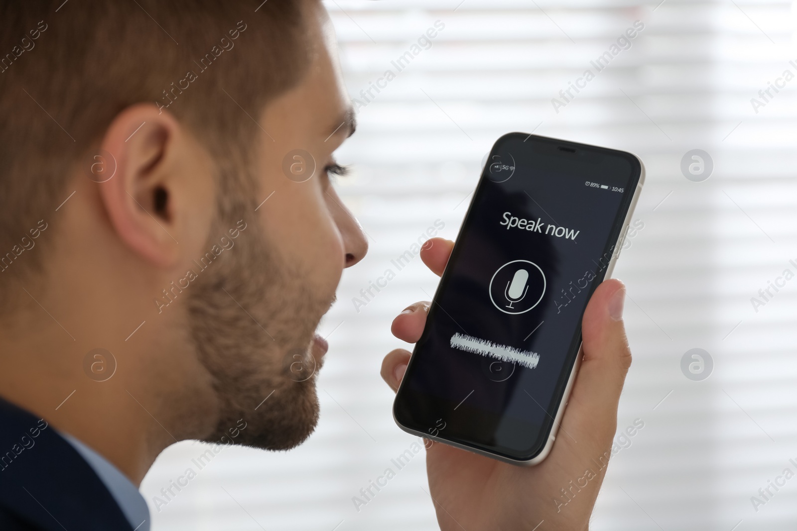 Photo of Young man using voice search on smartphone indoors, closeup