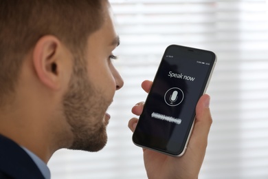 Photo of Young man using voice search on smartphone indoors, closeup
