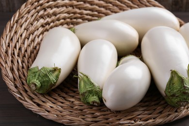 Photo of Fresh white eggplants in wicker basket on wooden table, closeup