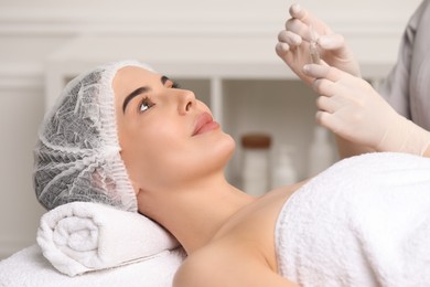 Photo of Professional cosmetologist holding skincare ampoule while working with client in clinic, closeup