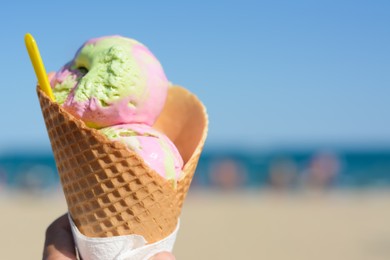 Photo of Little girl holding waffle cone with scoops of delicious colorful ice cream at beach on sunny summer day, closeup. Space for text