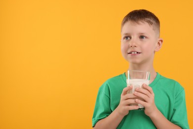 Cute boy with glass of fresh milk on orange background, space for text