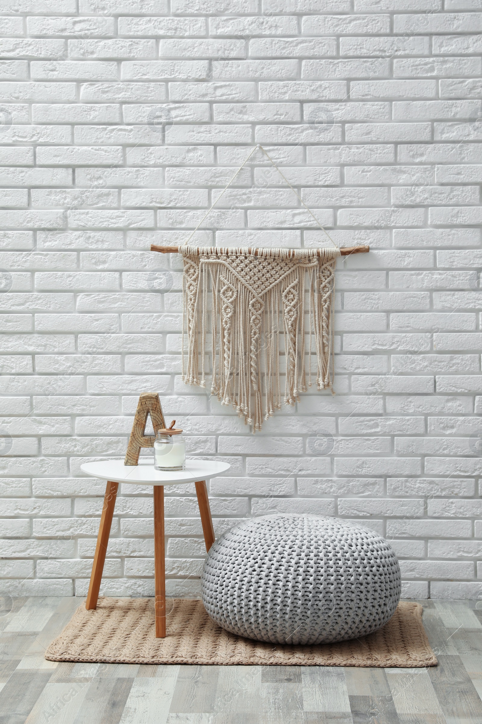 Photo of Comfortable knitted pouf, table and decor elements near white brick wall indoors. Interior design