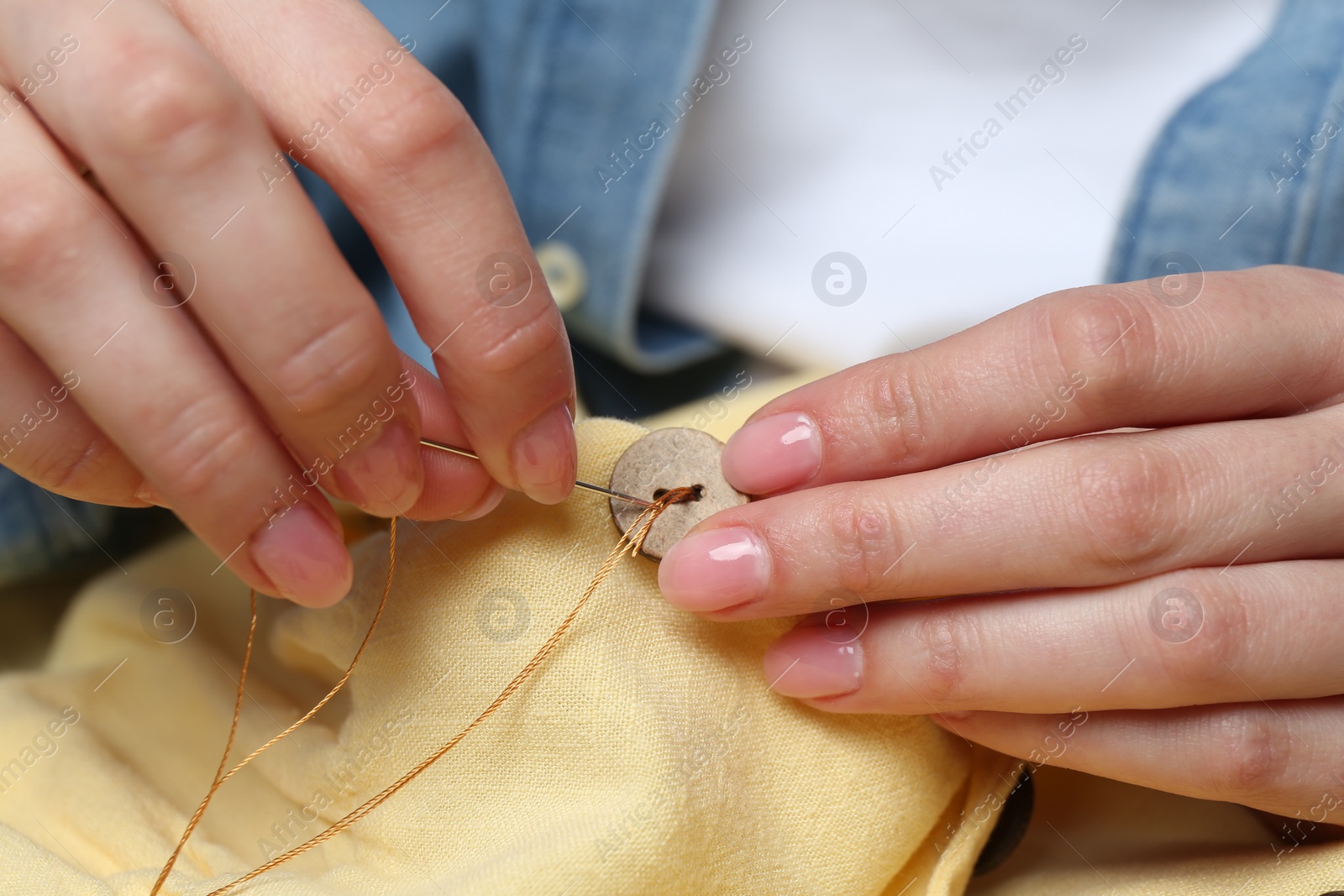 Photo of Woman sewing button with needle and thread onto shirt, closeup