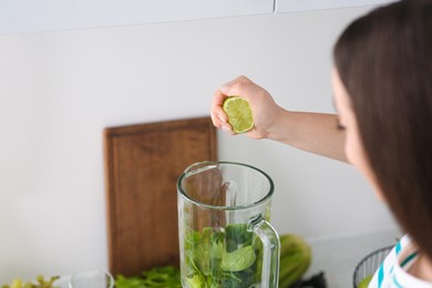 Photo of Woman adding lime juice into blender with ingredients for smoothie indoors, closeup