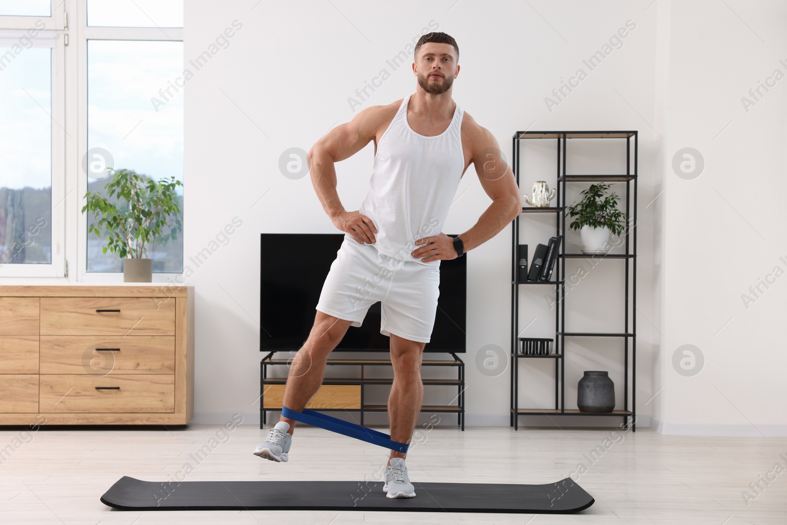 Photo of Athletic man doing exercise with elastic resistance band on mat at home