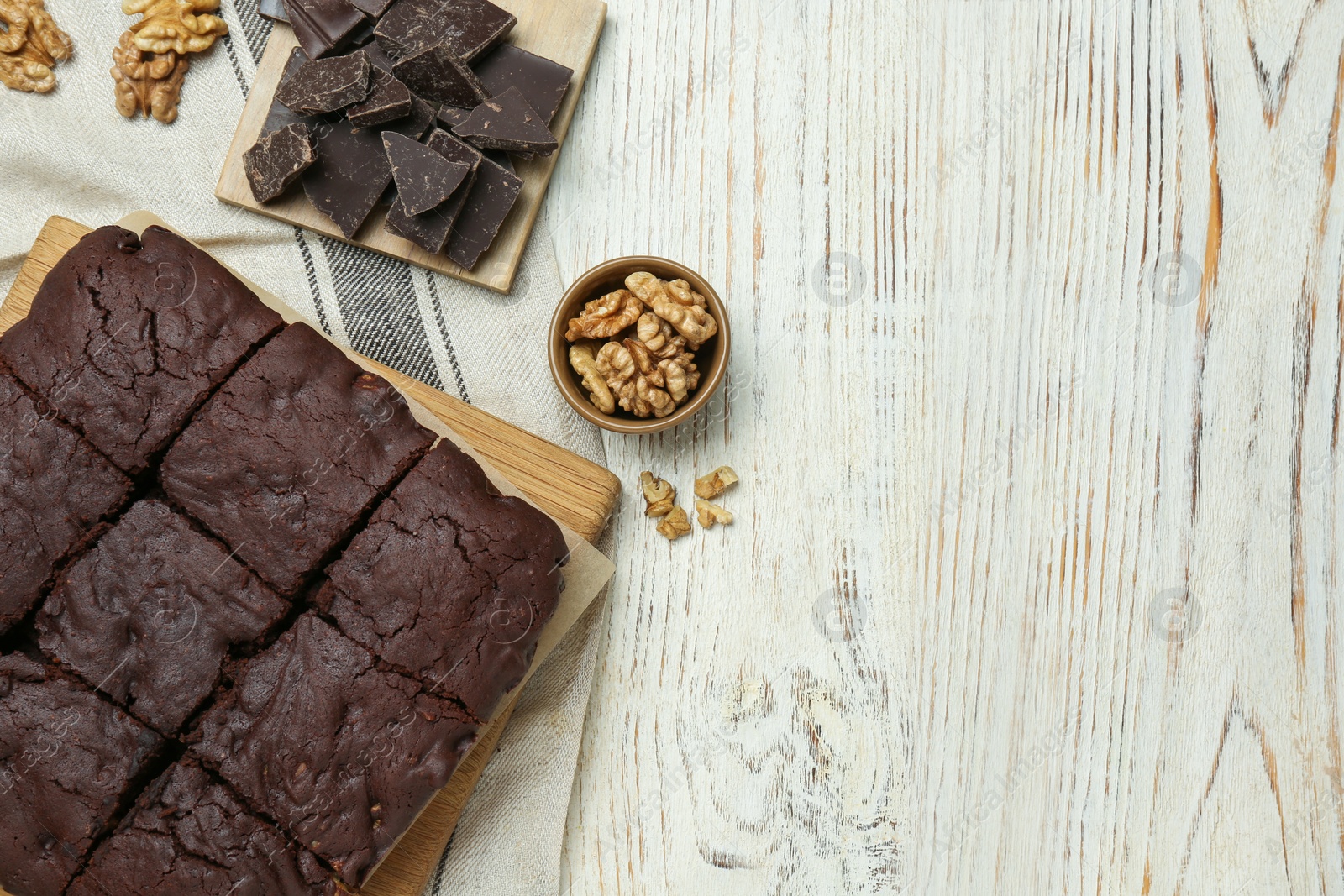 Photo of Delicious freshly baked brownies, walnuts and pieces of chocolate on white wooden table, flat lay. Space for text
