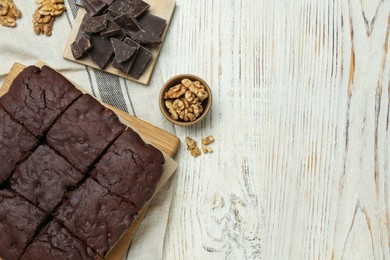 Delicious freshly baked brownies, walnuts and pieces of chocolate on white wooden table, flat lay. Space for text