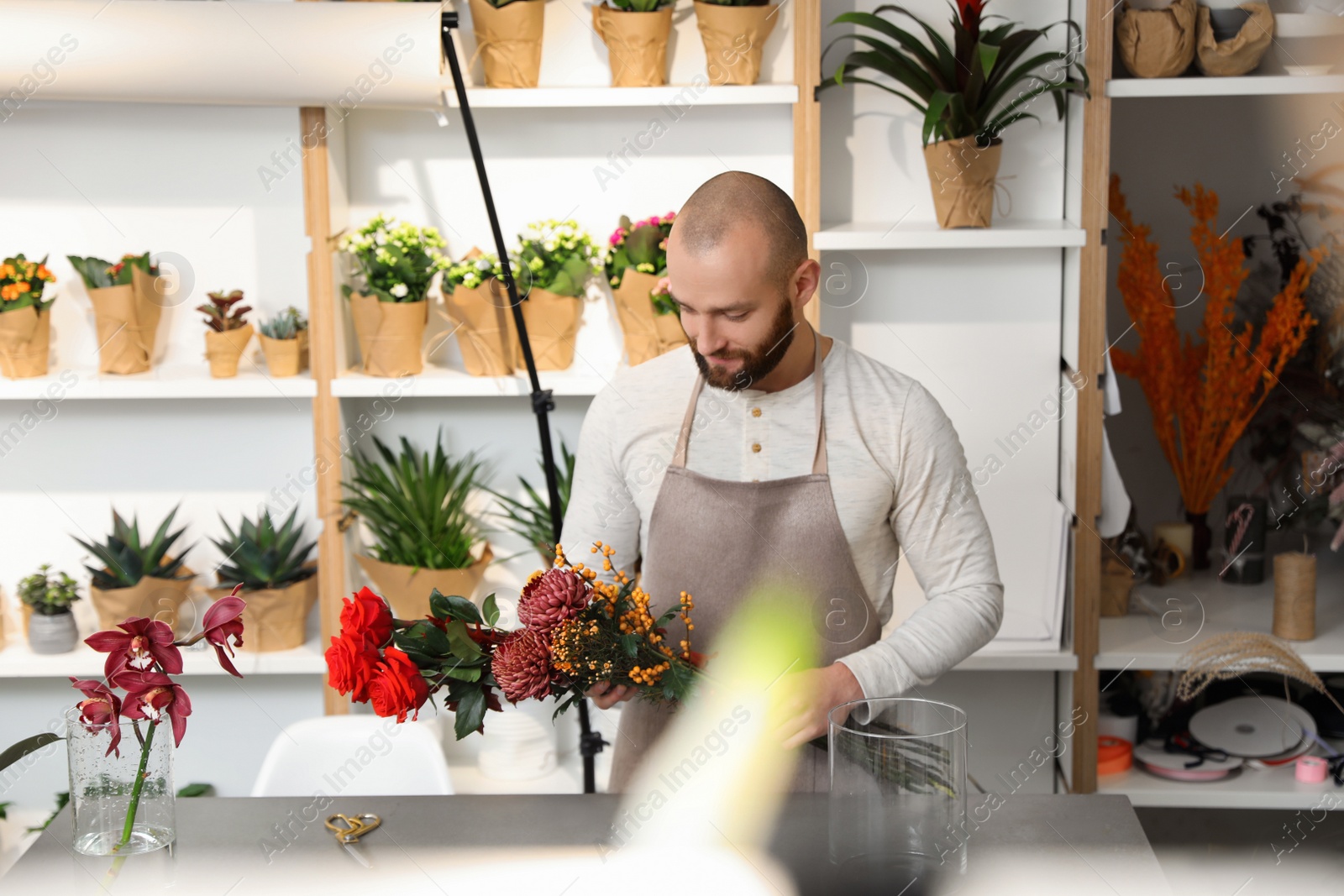 Photo of Florist making bouquet with fresh flowers at table in shop