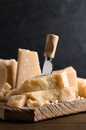 Photo of Parmesan cheese with board and knife on wooden table