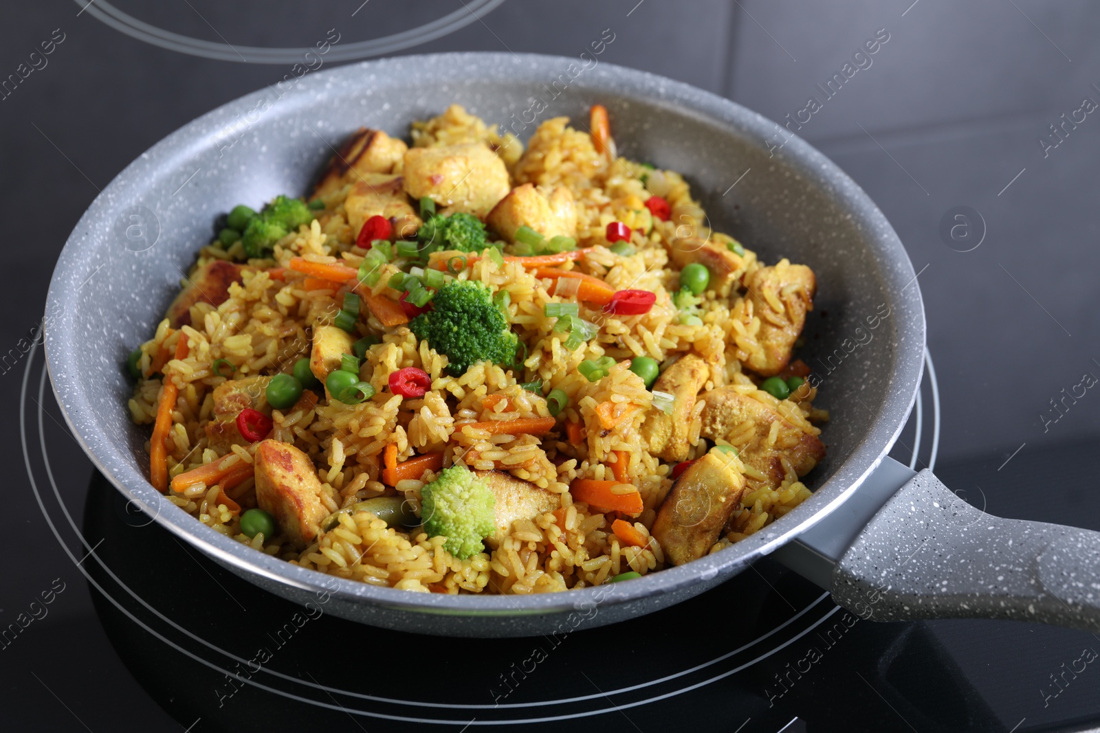 Photo of Tasty rice with meat and vegetables in frying pan on induction stove, closeup