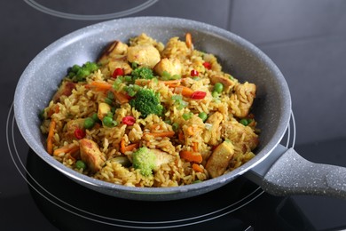 Photo of Tasty rice with meat and vegetables in frying pan on induction stove, closeup