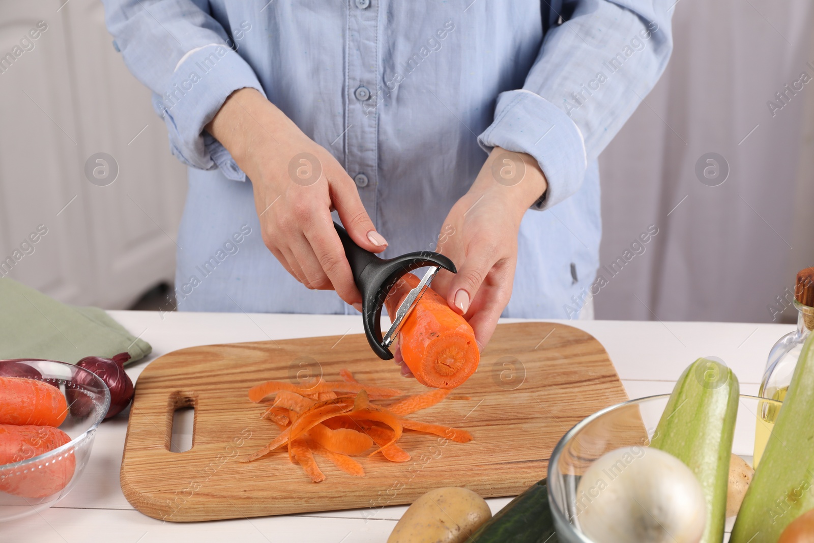 Photo of Woman peeling fresh carrot at white wooden table indoors, closeup