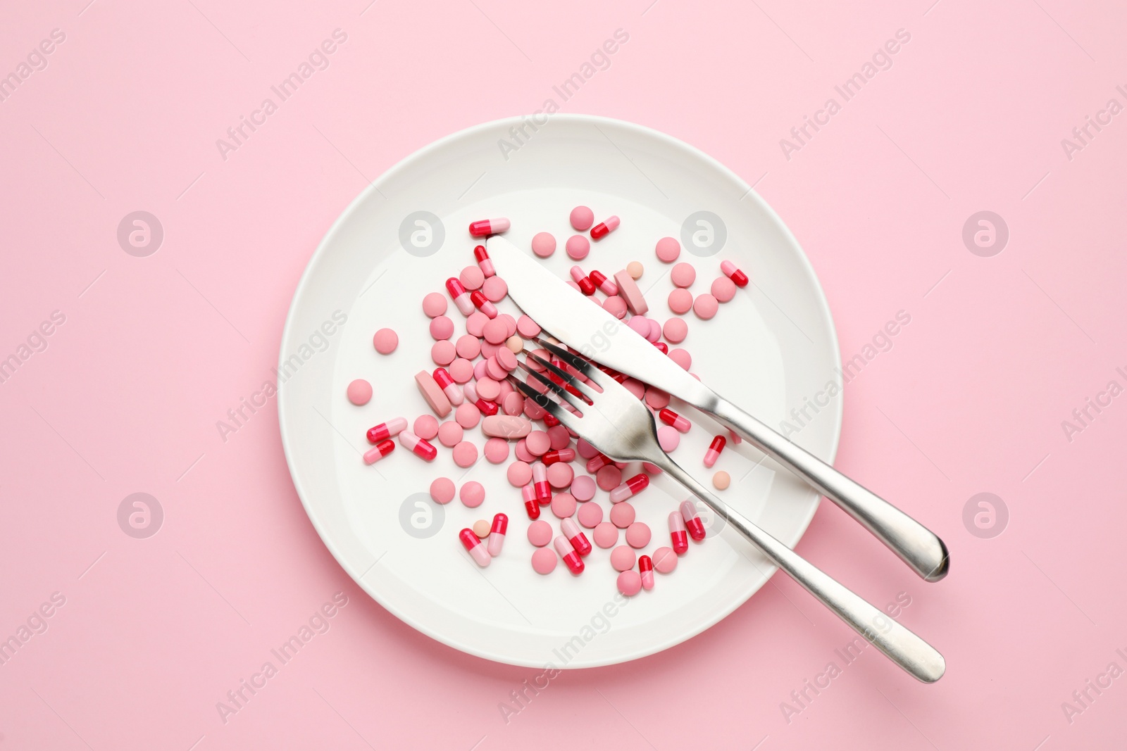 Photo of Plate with weight loss pills and cutlery on pink background, top view