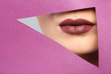 Photo of Lips of beautiful young woman with dark lipstick visible through hole in color paper