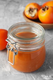 Photo of Delicious persimmon jam and fresh fruits on grey table
