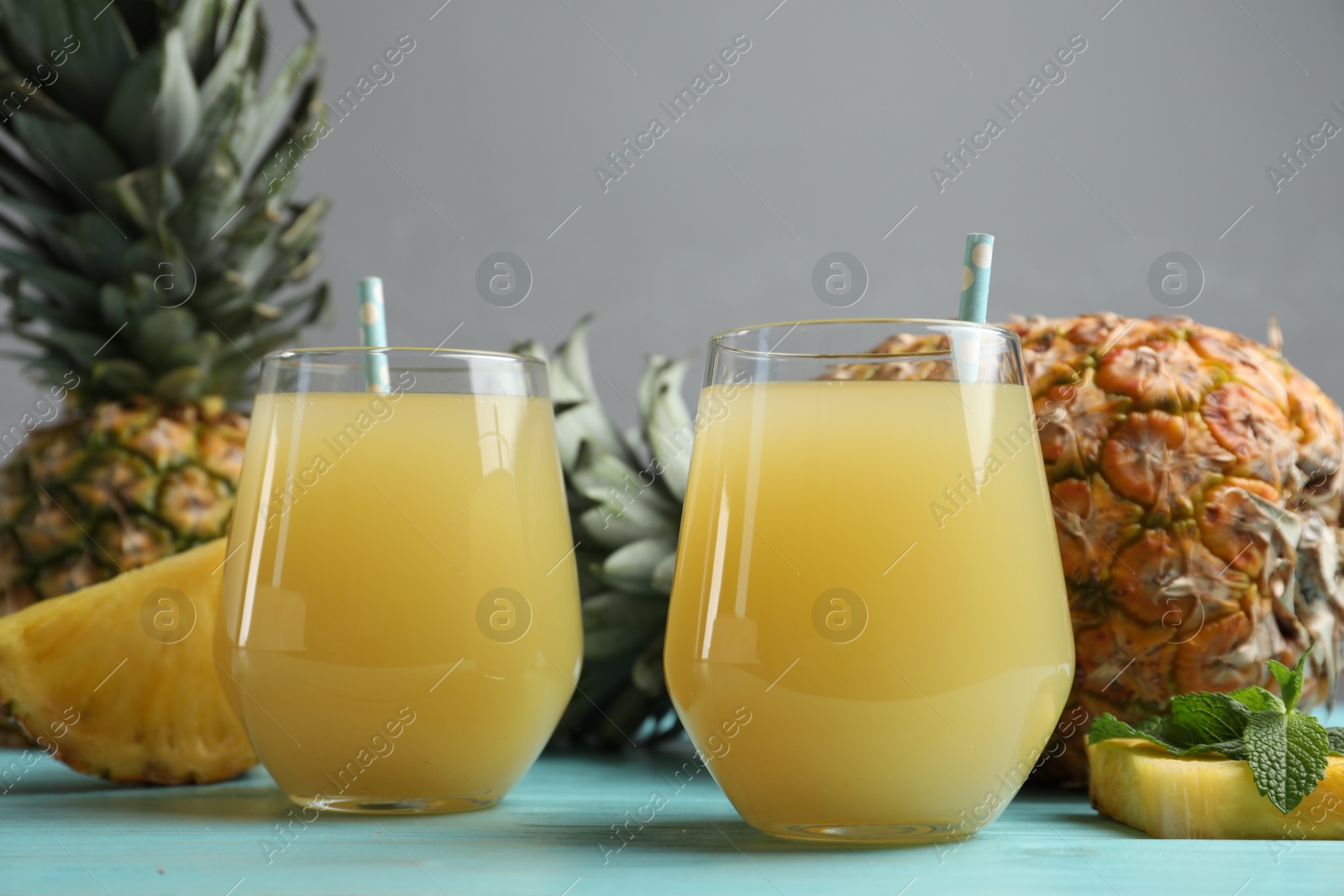 Photo of Delicious pineapple juice and fresh fruit on light blue wooden table