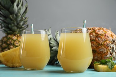 Photo of Delicious pineapple juice and fresh fruit on light blue wooden table