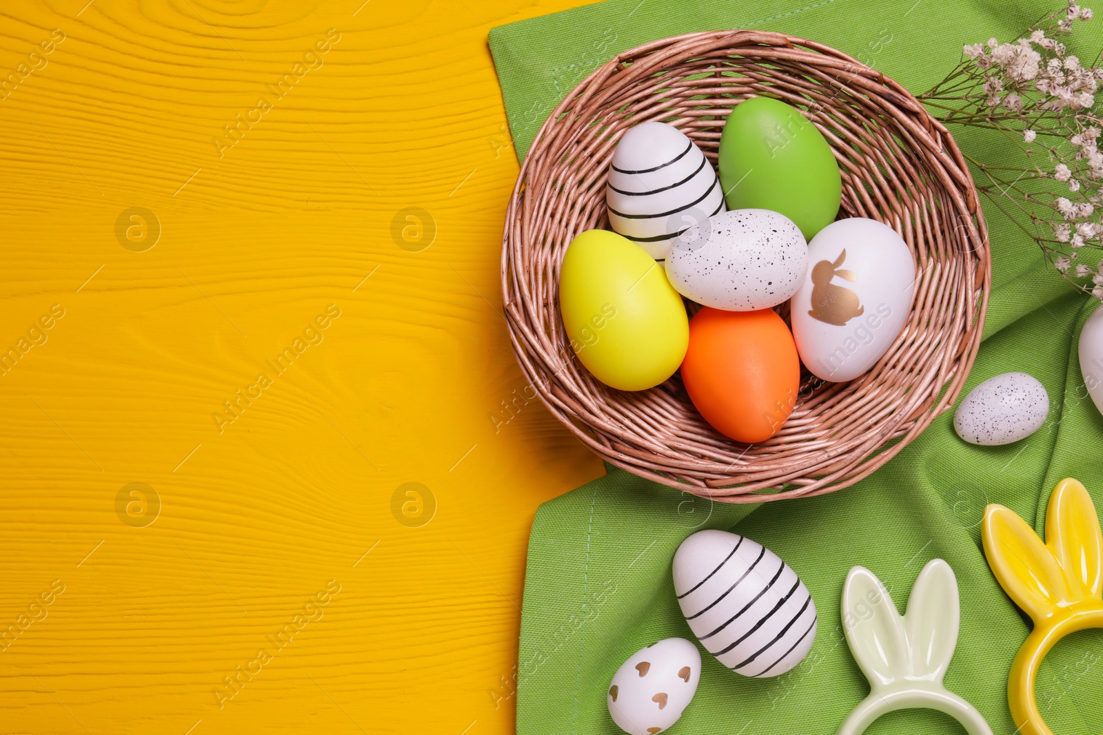 Photo of Flat lay composition with painted eggs, and Easter decorations on yellow wooden table. Space for text