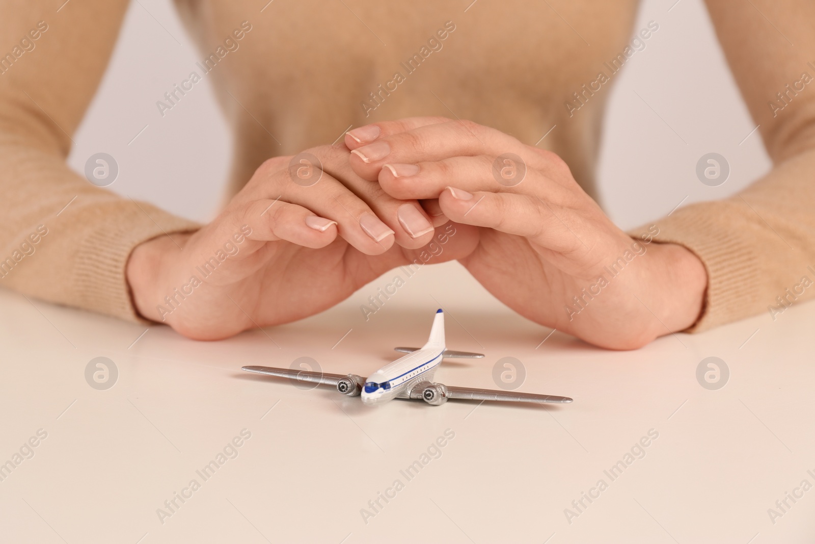 Photo of Woman covering toy plane at table, closeup. Travel insurance concept