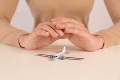 Photo of Woman covering toy plane at table, closeup. Travel insurance concept