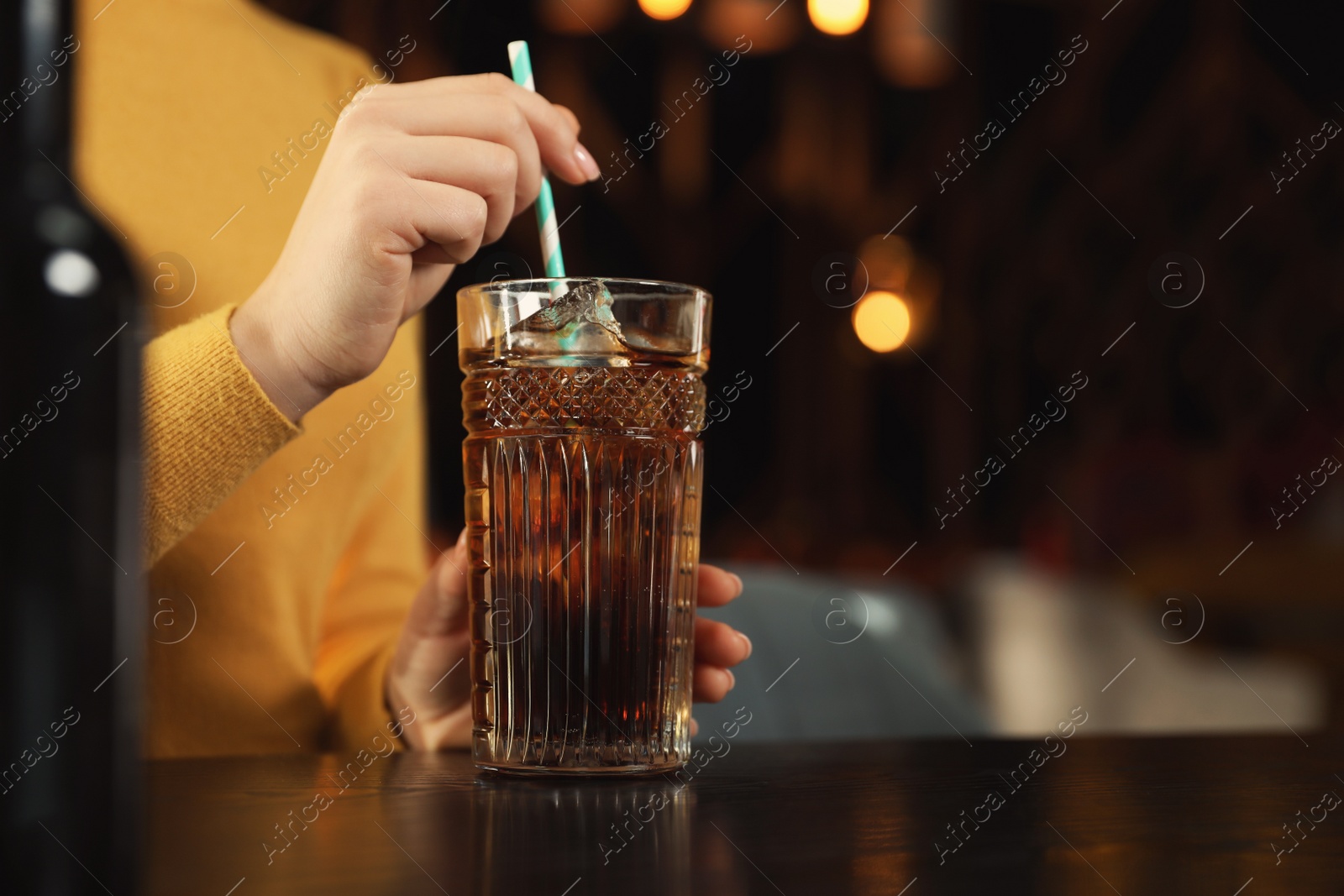 Photo of Woman with glass of refreshing cola at table indoors, closeup. Space for text