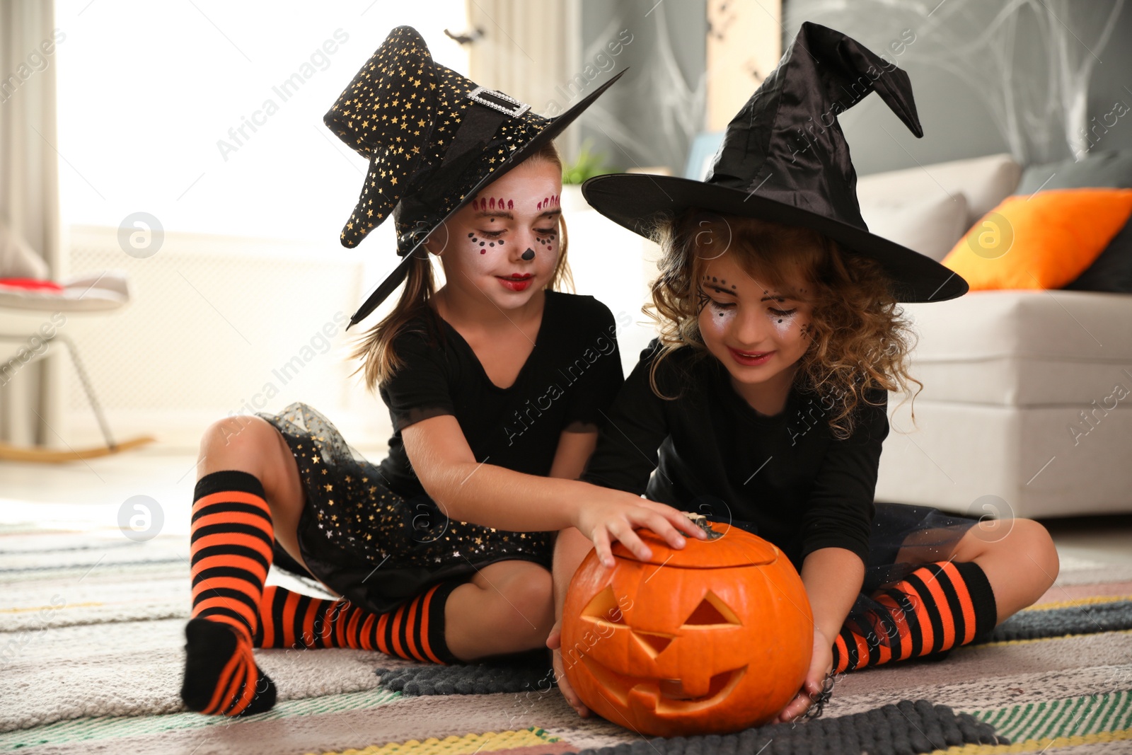 Photo of Cute little girls with pumpkin head jack lantern wearing Halloween costumes at home