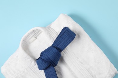 Karate belt and white kimono on light blue background, top view