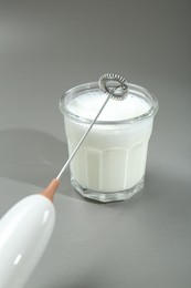 Photo of Mini mixer (milk frother) and whipped milk in glass on grey background