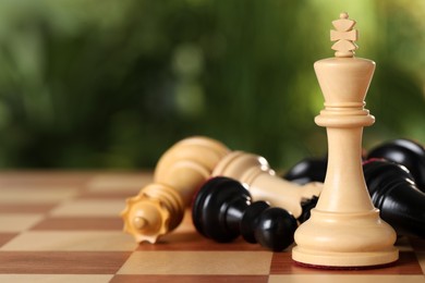 Photo of Wooden king among fallen chess pieces on game board against blurred background, closeup. Space for text