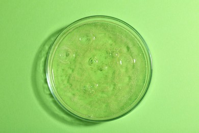 Photo of Petri dish with liquid sample on green background, top view