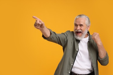 Photo of Happy senior sports fan pointing on yellow background, space for text